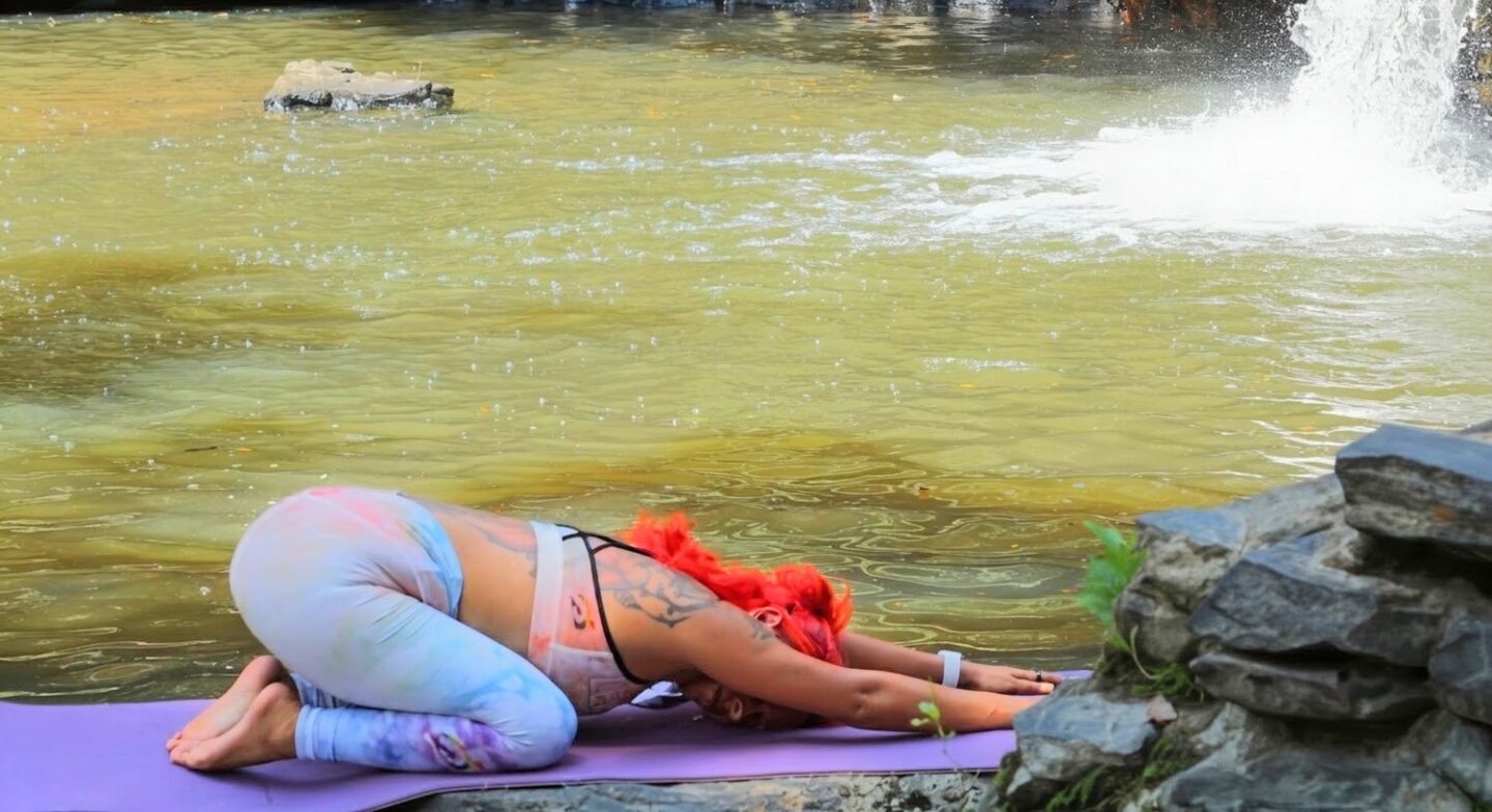 Woman resting in child's pose (Balasana) on a yoga mat by the water